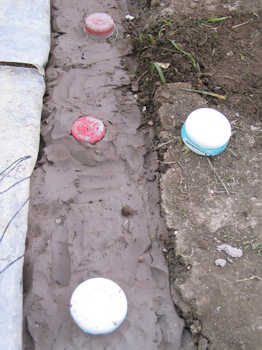 17. A close up of the milk bottle tops. The wires are under the upturned yoghurt pot to the right.
